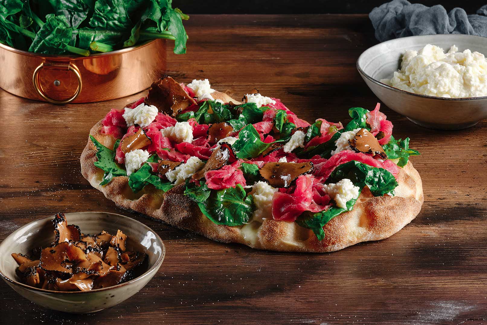 Pinsa pinsami con mozzarella julienne, foglie di spinacino, carpaccio di fassona, straccetti di mozzarella e petali di tartufo