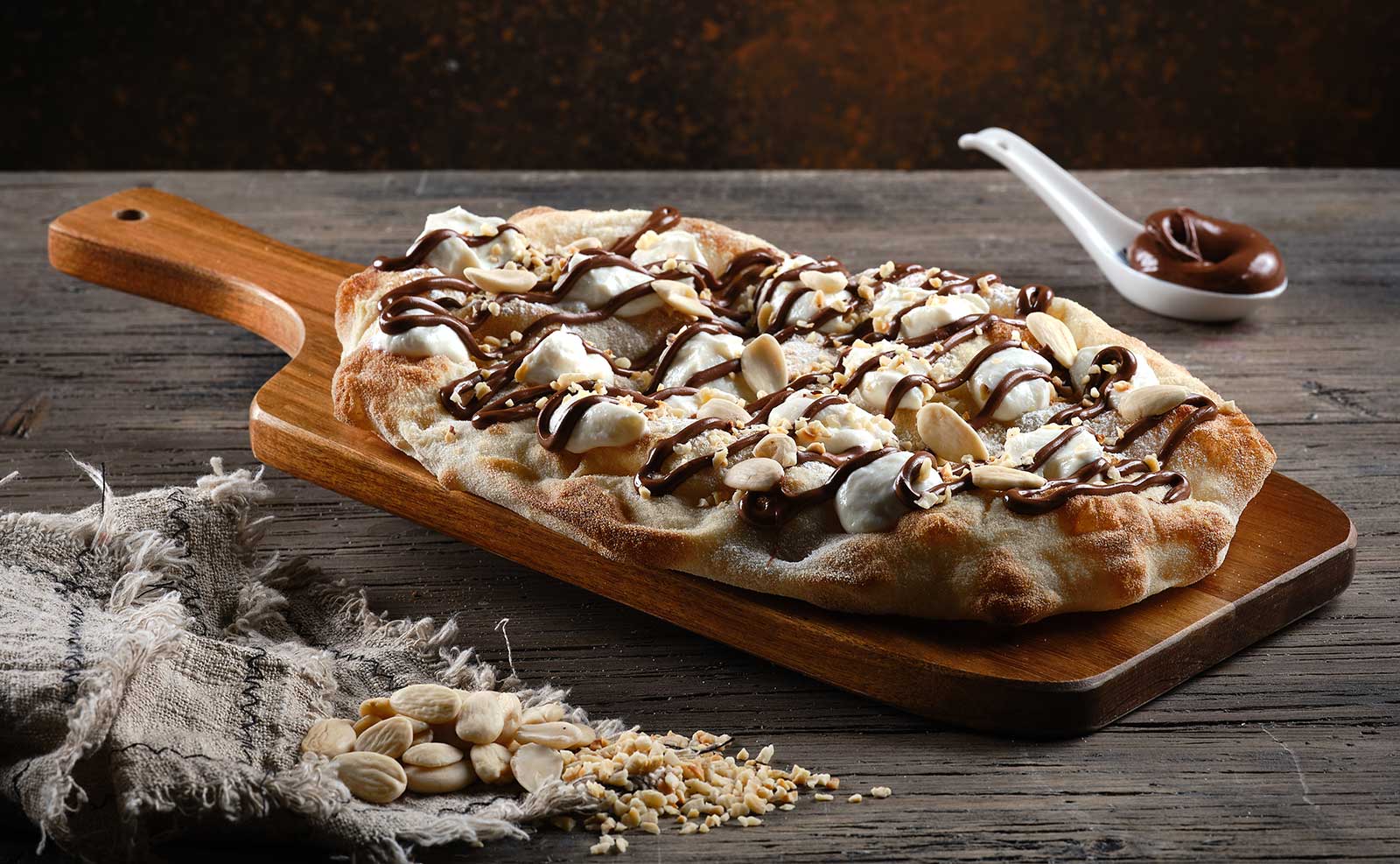 Pinsa garnished with hazelnut cream, chopped hazelnuts, peeled almonds and sweet ricotta