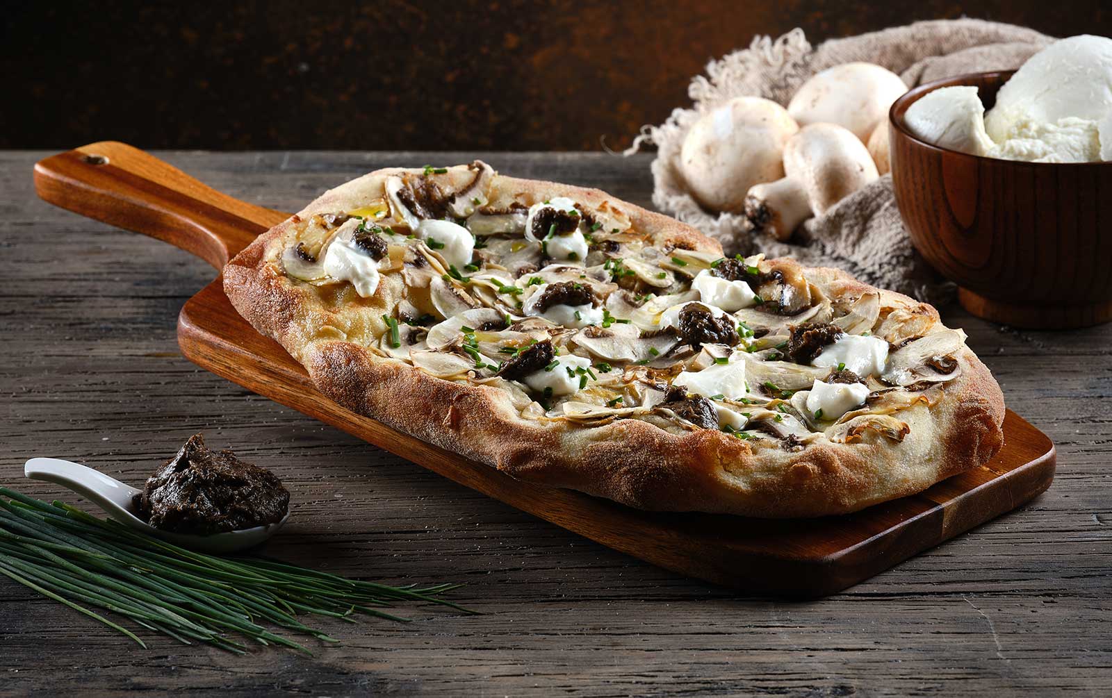 Pinsa garnished with mozzarella, truffle ceam, button mushrooms, ricotta and chives