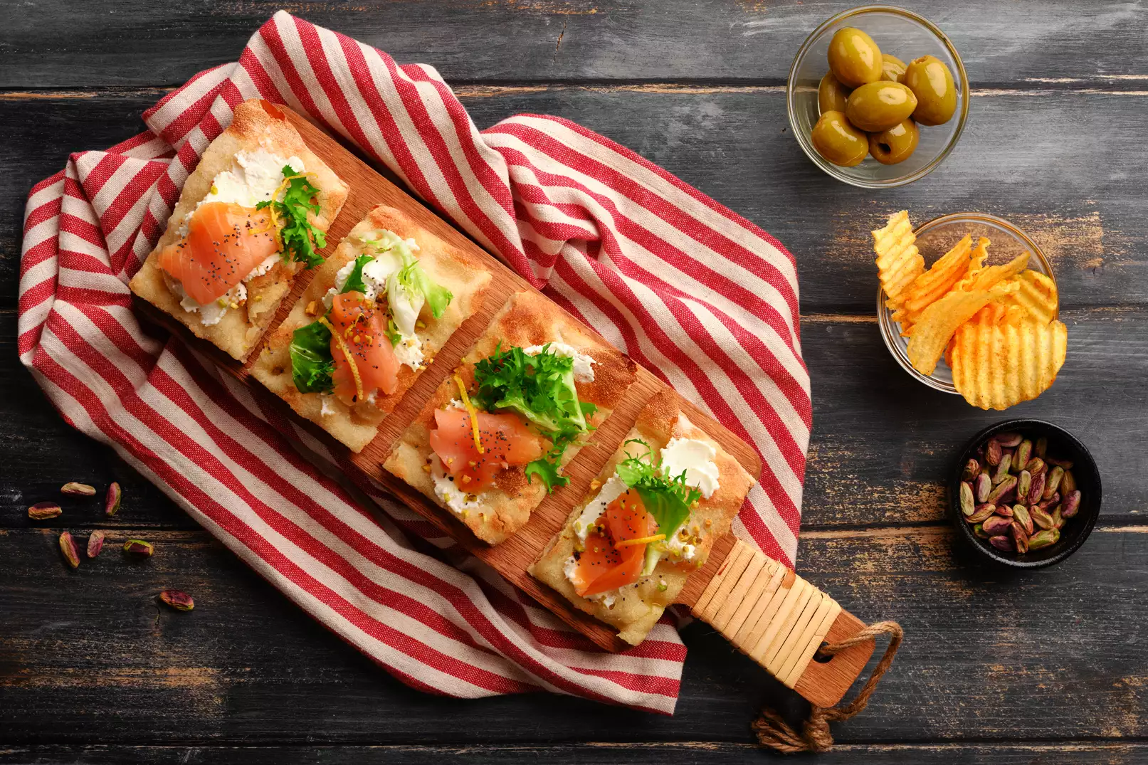 Pinsa con formaggio spalmabile, insalata, salmone, pistacchio, zeste di limone e semi di papavero