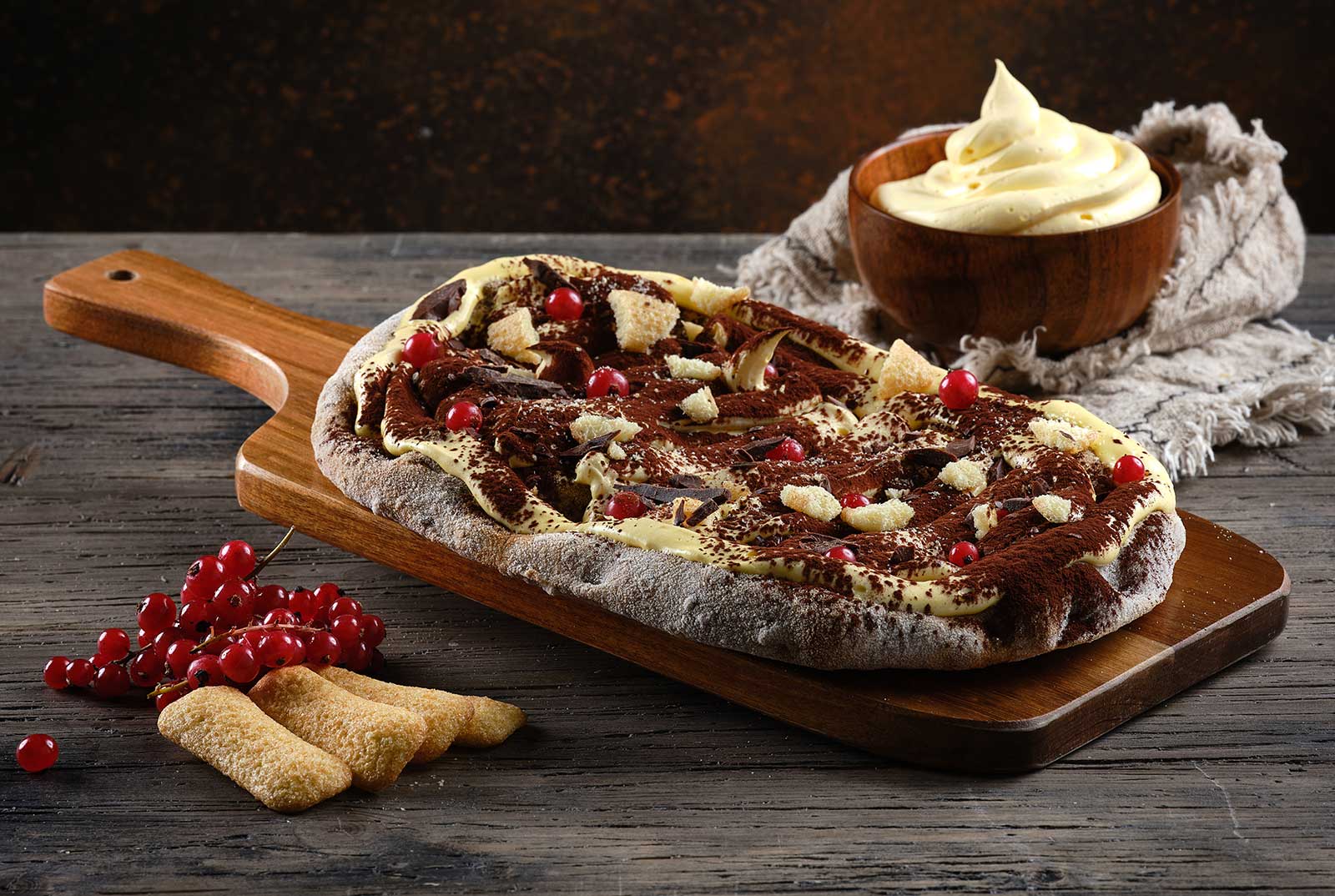 Coffee-soaked pinsa pinsami garnished with mascarpone cream, chocolate, cocoa, red currants and dry cookies