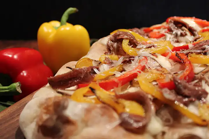 Backe die Pinsa im vorgeheizten Ofen für etwa 5-7 Minuten und füge nach dem Backen die Sardellenfilets hinzu. Reibe den Pecorino darüber.