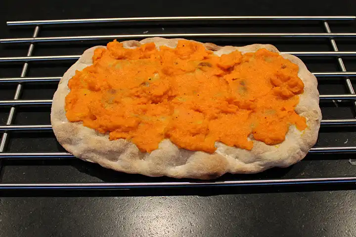 Platziere die Pinsa-Basis auf einem Rost und verteile die Karottencreme