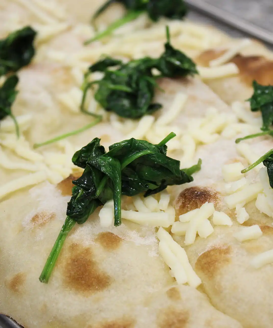 Beginne die Pinsa-Basis mit Mozzarella und dem angeschwitzten Spinat zu belegen.