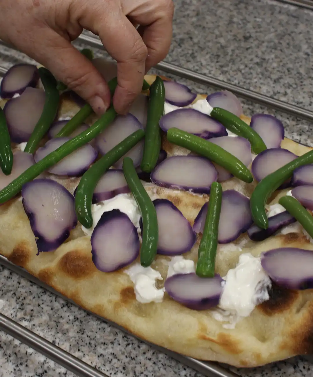 Stendi la base pinsa su una griglia ed aggiungi patate viola e fagiolini