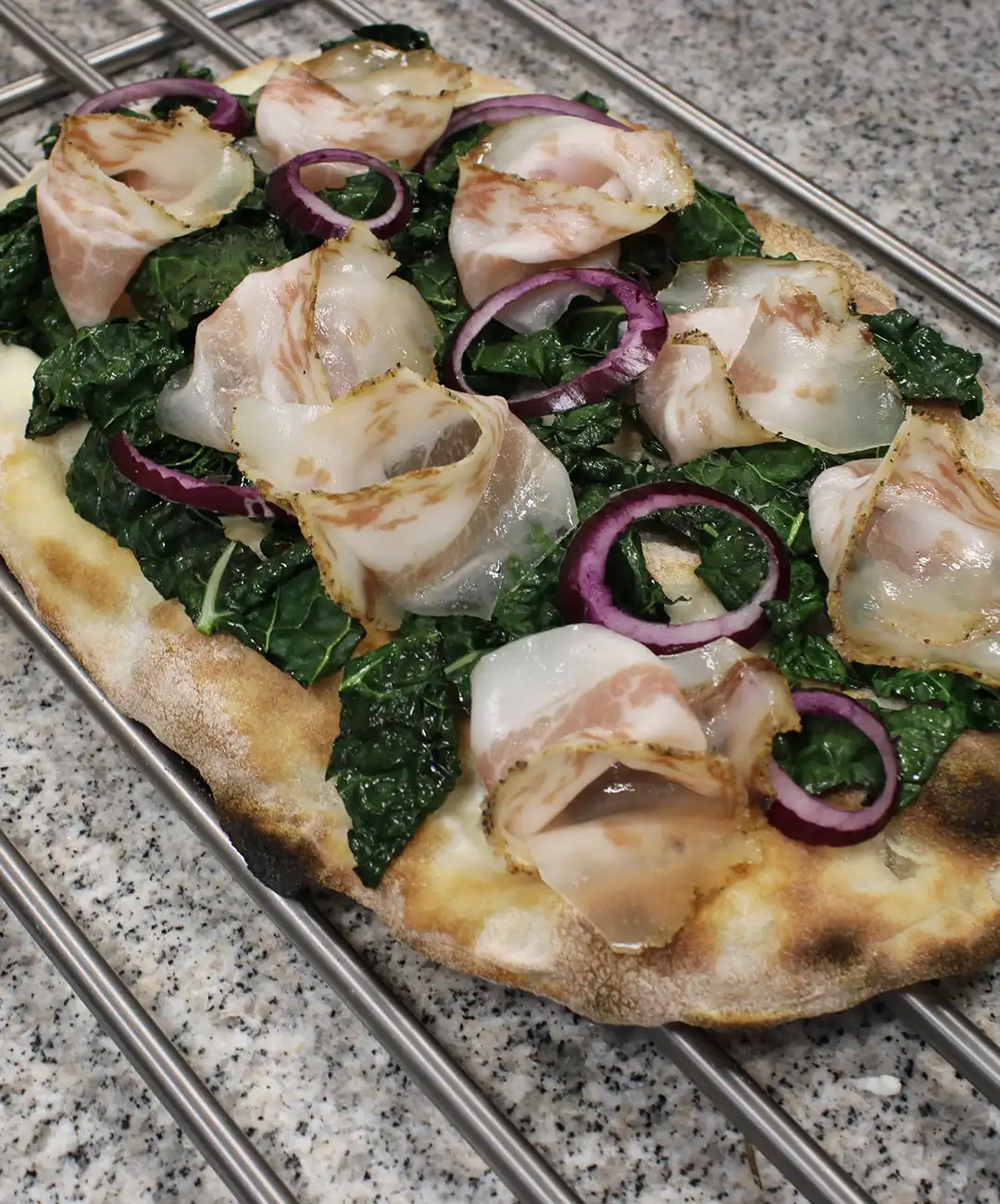 Verteile den Mozzarella auf der gesamten Pinsa-Grundlage, füge den zuvor gekochten Grünkohl, das Guanciale und die Zwiebel hinzu