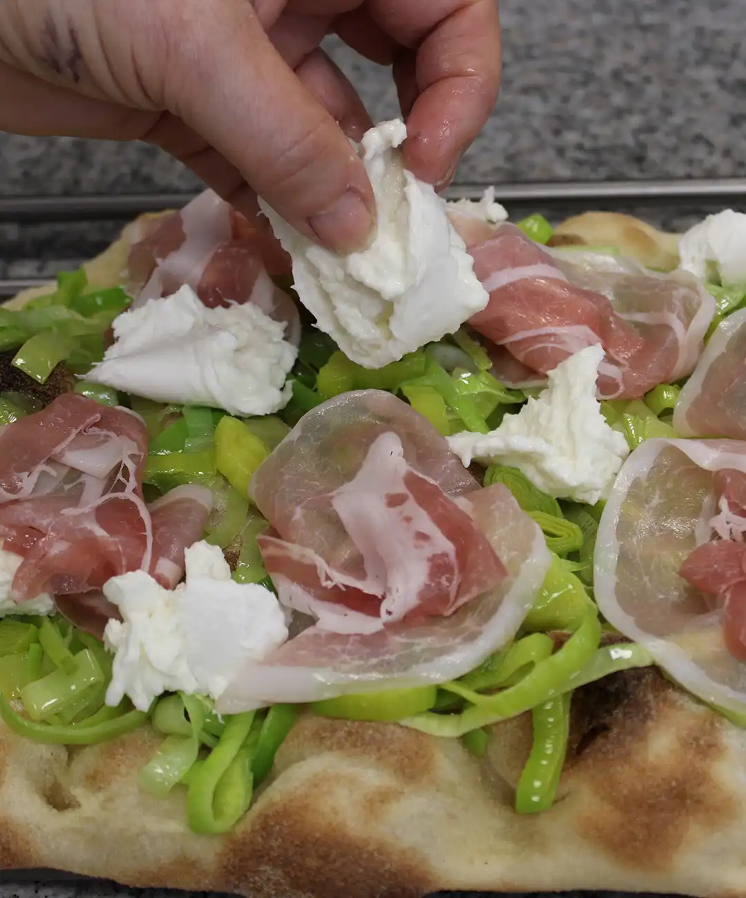 Metti la pinsa su una griglia ed aggiungi pancetta, mozzarella di bufala e porro