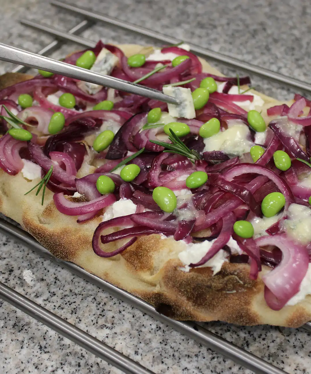 Metti la pinsa sulla griglia ed aggiungi la cipolla, gorgonzola e edamame