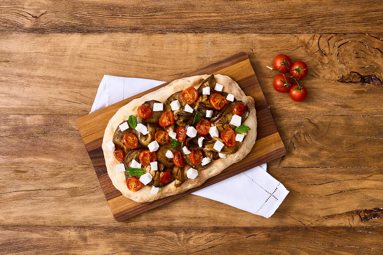 Una Pinsa a base di melanzane grigliate, pomodori confit e feta vegana