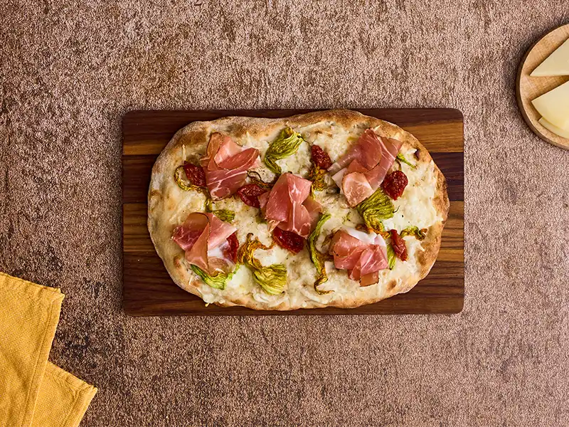 Completa con gli ultimi ingredienti la pinsa con fiori di zucca e caciocavallo