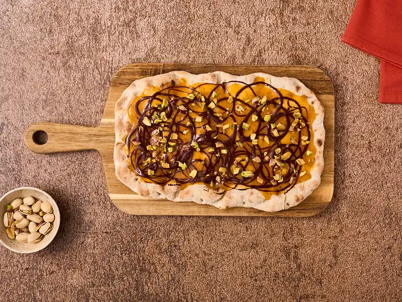 Completa la ricetta pinsa con crema di cachi, cioccolato fondente e pistacchi