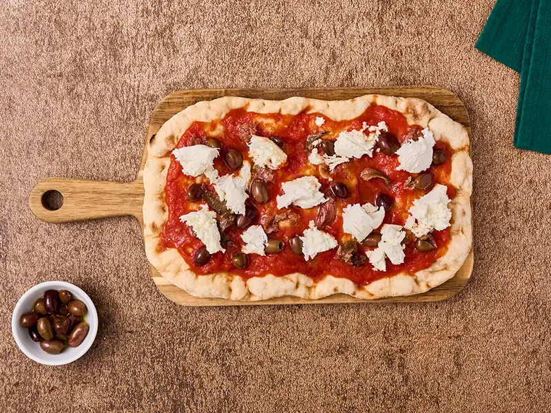 Stendi la passata di pomodoro, le acciughe sott'olio e gli altri ingredienti sulla pinsa